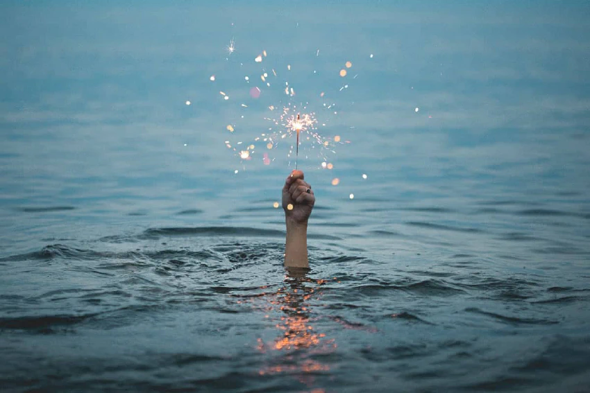 Hand sticking out of the water and holding a sparkler