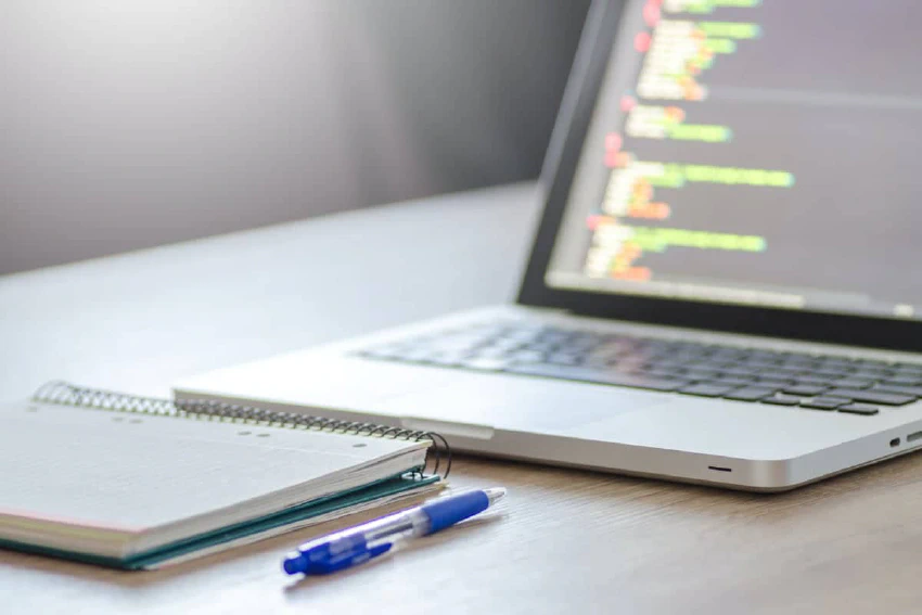 Laptop with code, notebook, and pen